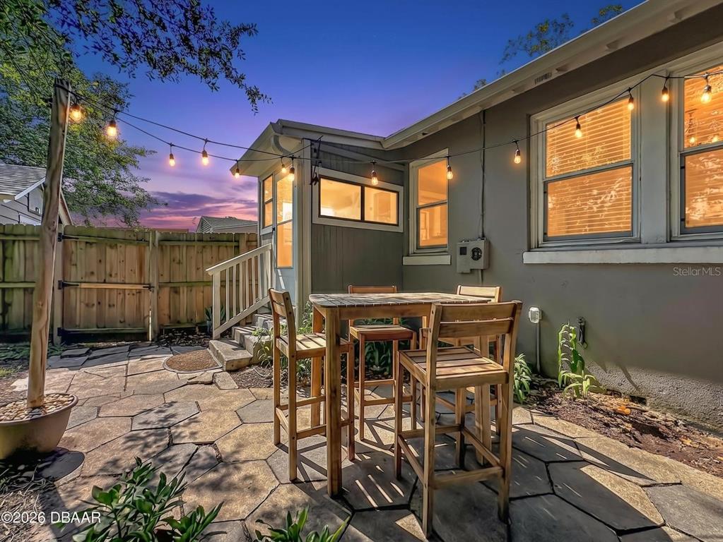 A stone patio features a wooden high-top table set beside a house with string lights — 2615 RIDGEWOOD ROAD, JACKSONVILLE, FL