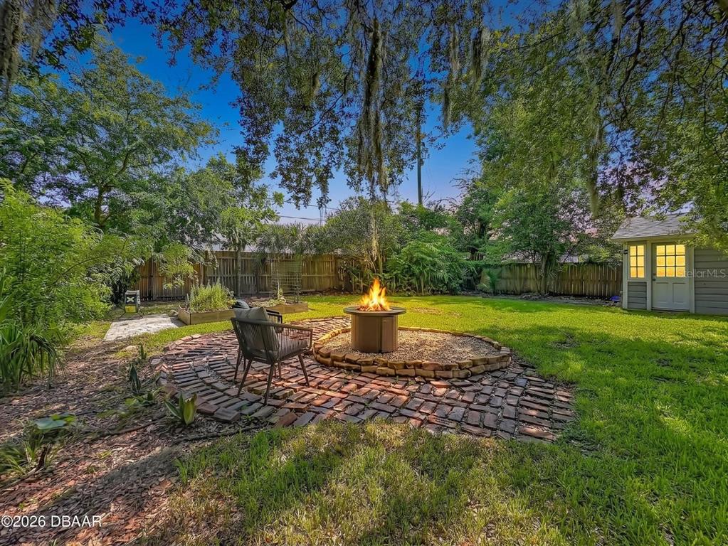 A backyard features a brick patio with a fire pit, a chair, and a shed — 2615 RIDGEWOOD ROAD, JACKSONVILLE, FL