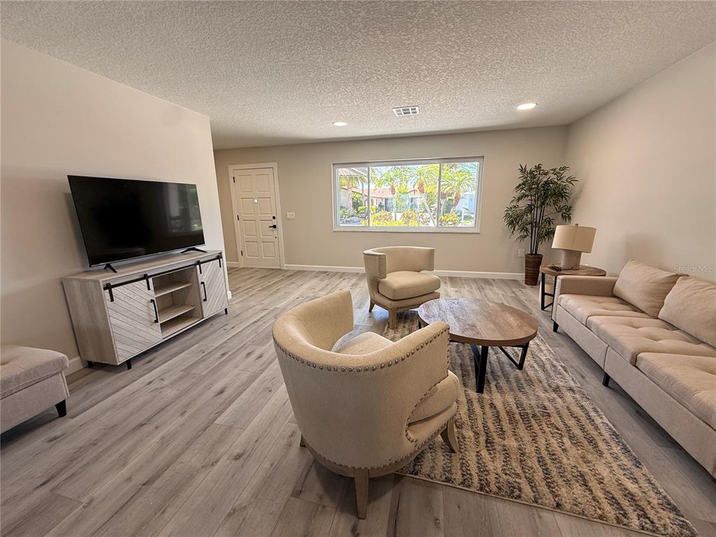 A living room features light wood-look flooring, a beige sofa, two armchairs, and a television — 4980 GALLEON COURT, NEW PORT RICHEY, FL