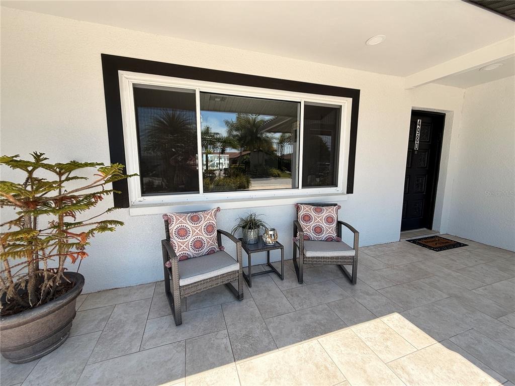 A covered patio features tiled flooring, two chairs with patterned pillows, and a large window — 4980 GALLEON COURT, NEW PORT RICHEY, FL