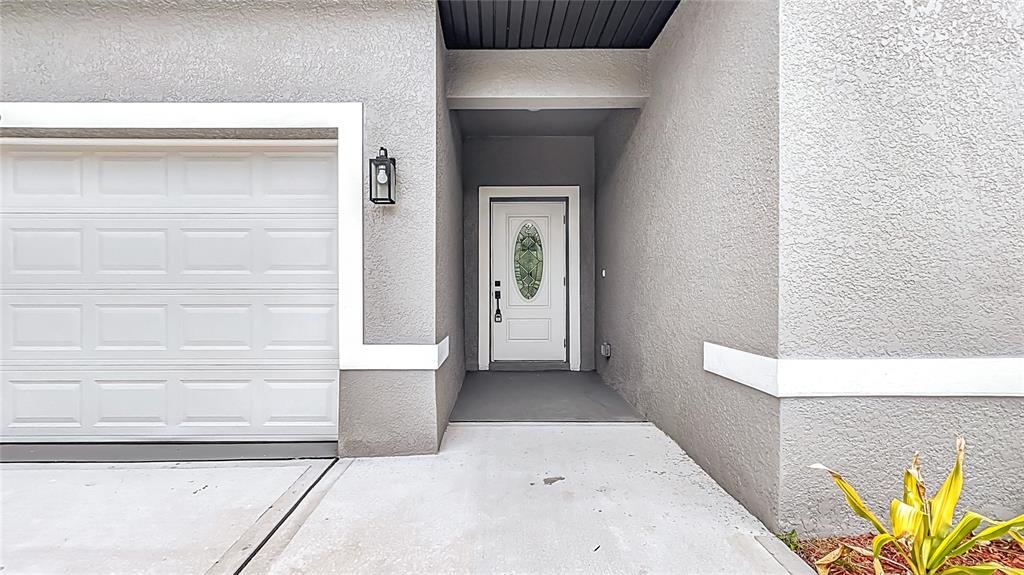 A white front door with a decorative glass insert sits beside a white garage door — 2391 YANKEE TERRACE, NORTH PORT, FL
