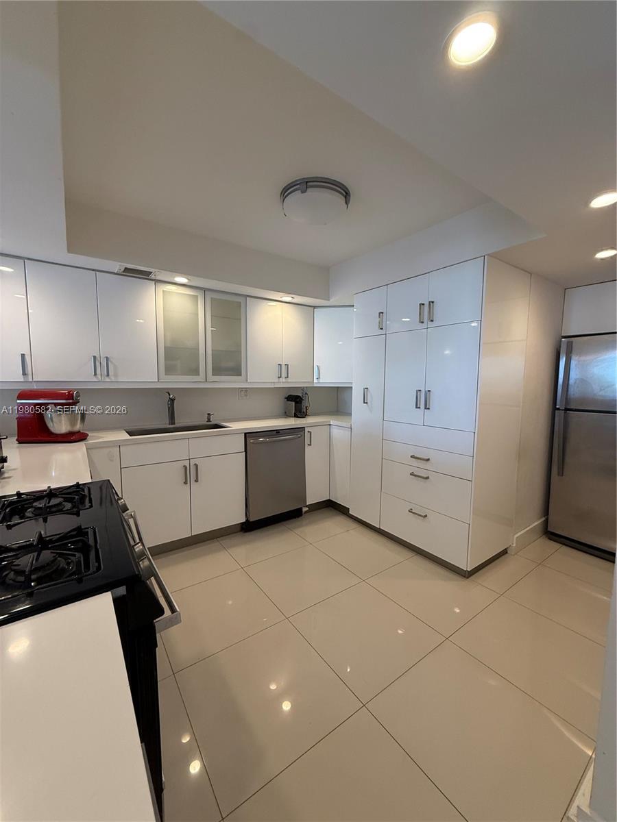 A modern kitchen features white glossy cabinets, stainless steel appliances, and light-colored tile flooring — 3140 S Ocean Dr # 310, Hallandale Beach FL 33009, HALLANDALE BEACH, FL