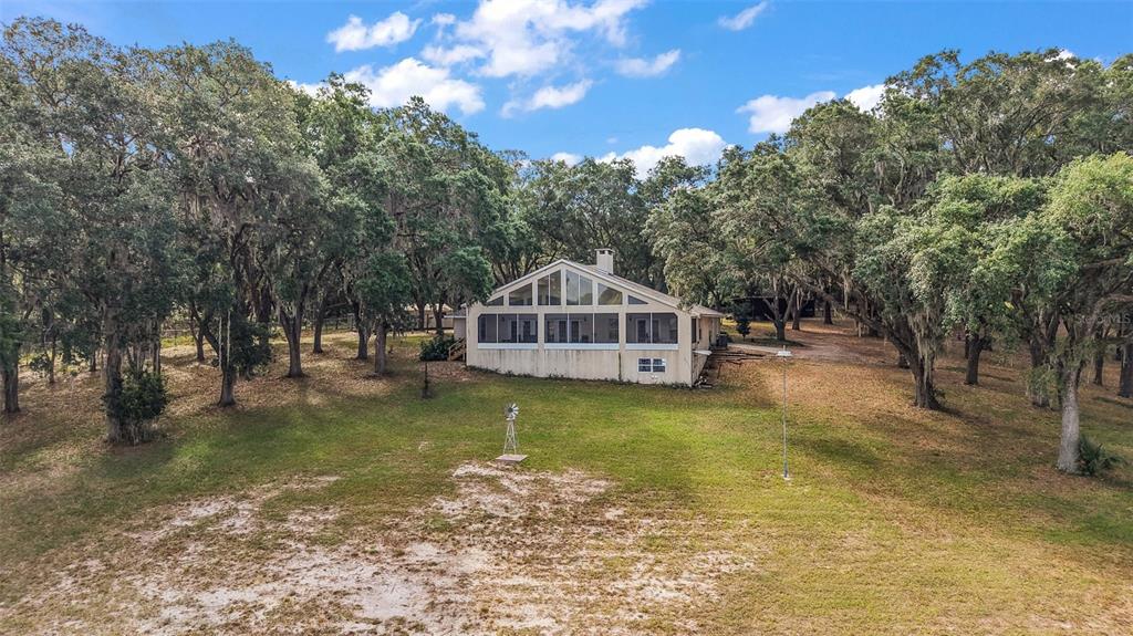 A beige house with a large screened-in porch and triangular windows sits in a wooded yard — 27011 SE HIGHWAY 42, UMATILLA, FL