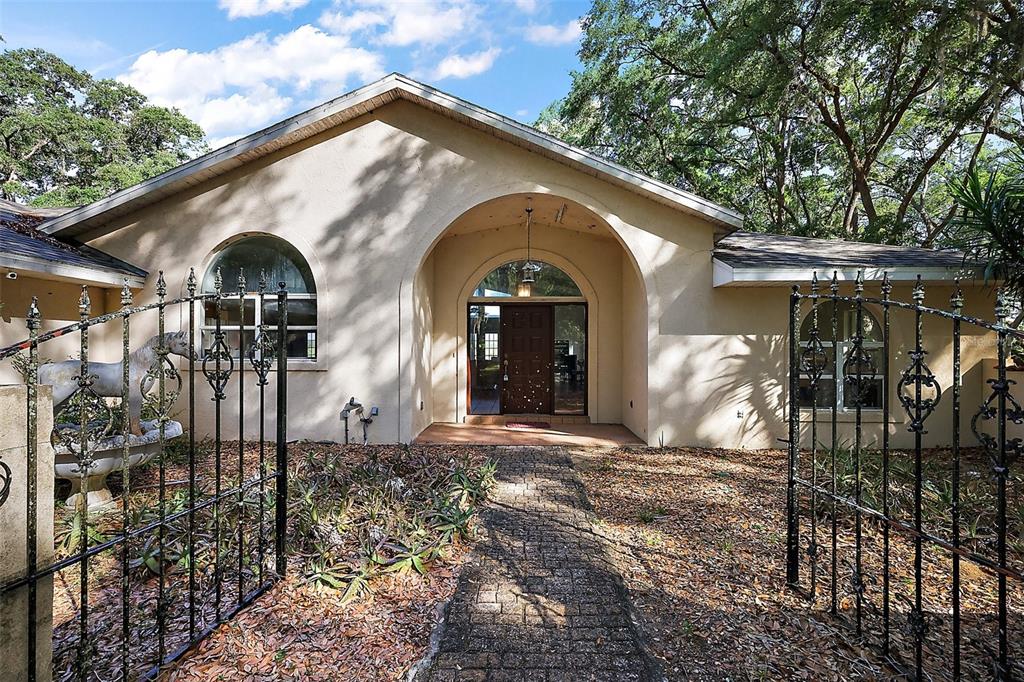 A beige house with an arched entryway and a gated brick walkway leading to the door — 27011 SE HIGHWAY 42, UMATILLA, FL