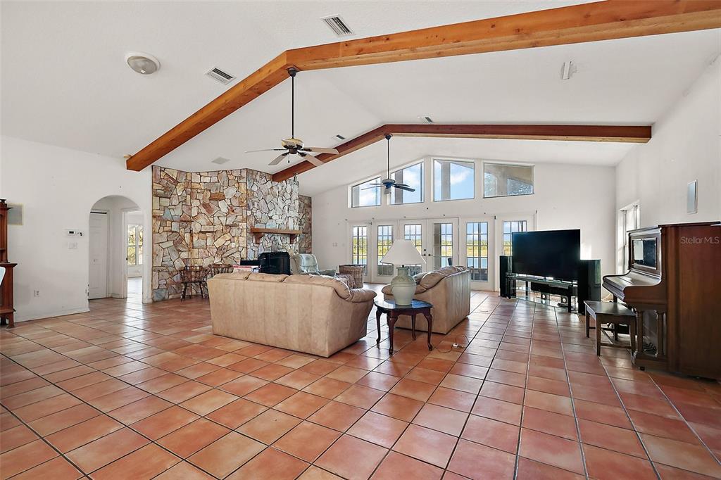 A spacious living room features vaulted ceilings with exposed wood beams, tile floors, and stone fireplace — 27011 SE HIGHWAY 42, UMATILLA, FL