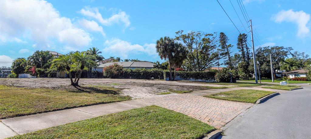 A vacant residential lot features a paved driveway apron, sidewalk, and various trees and shrubs — 105 ESTADO WAY NE, ST PETERSBURG, FL