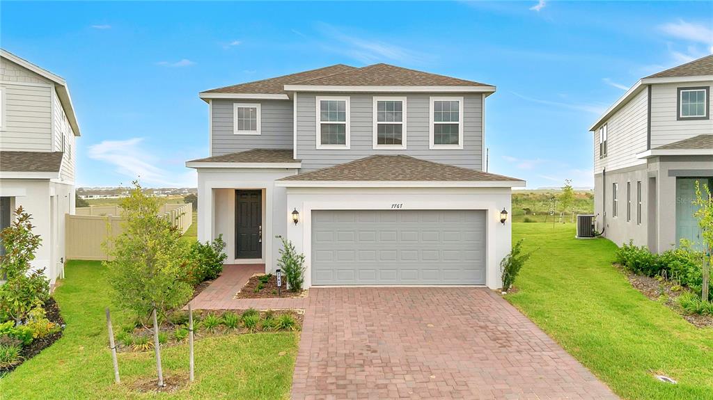 A two-story suburban house with a gray garage, light siding, and a brick driveway — 7767 TRAPANI LOOP, CLERMONT, FL