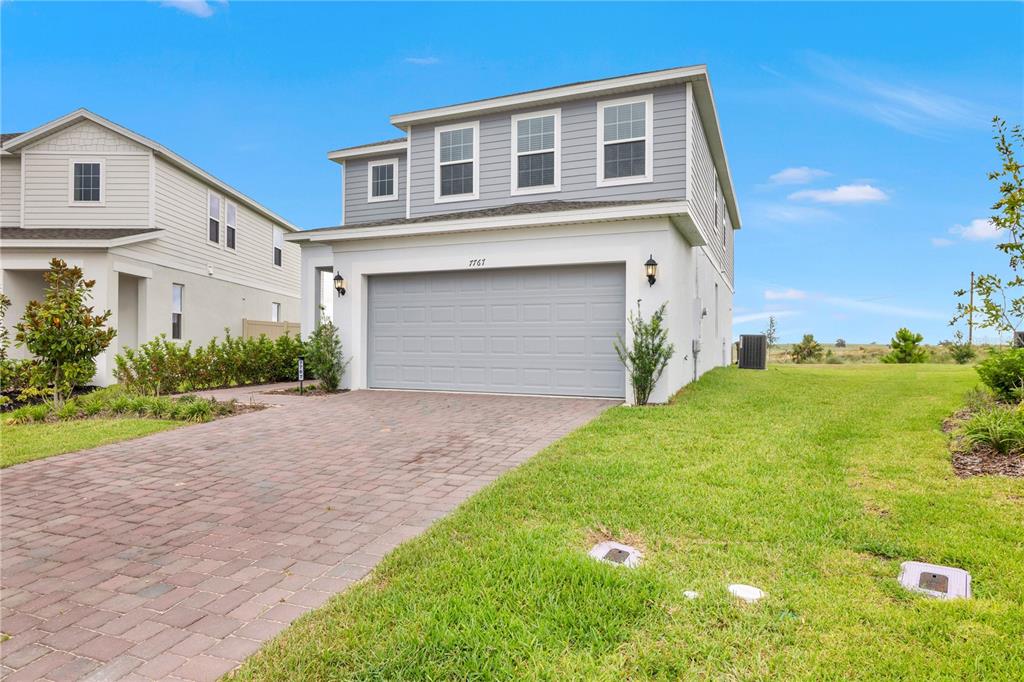 A two-story house with a gray garage door, white stucco, and gray siding — 7767 TRAPANI LOOP, CLERMONT, FL