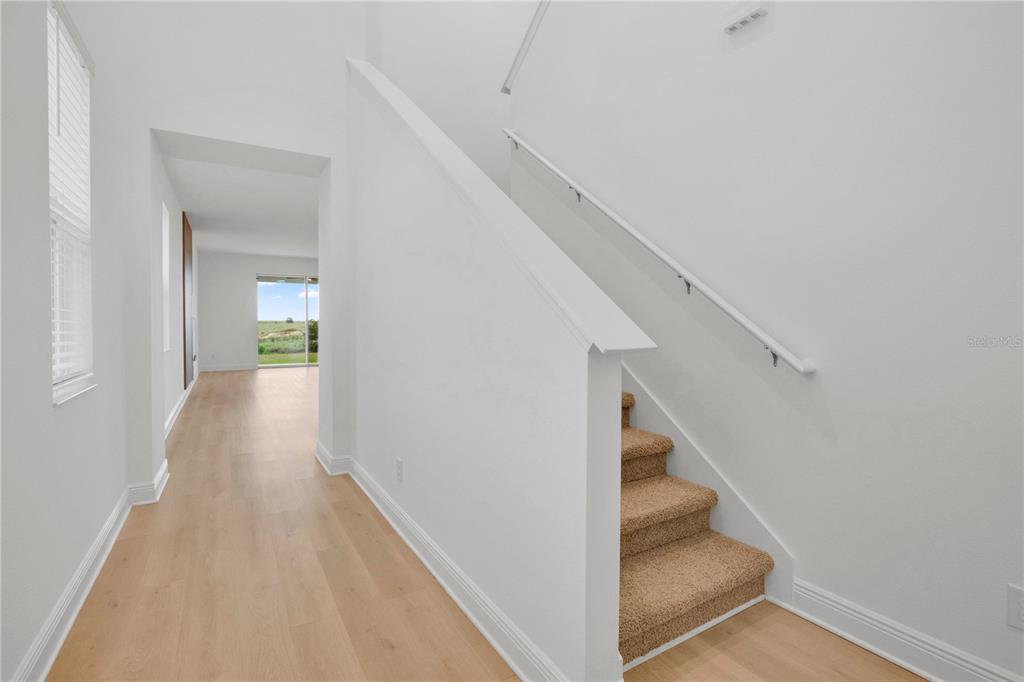 A hallway with light wood flooring leads to a doorway with a view of grass — 7767 TRAPANI LOOP, CLERMONT, FL