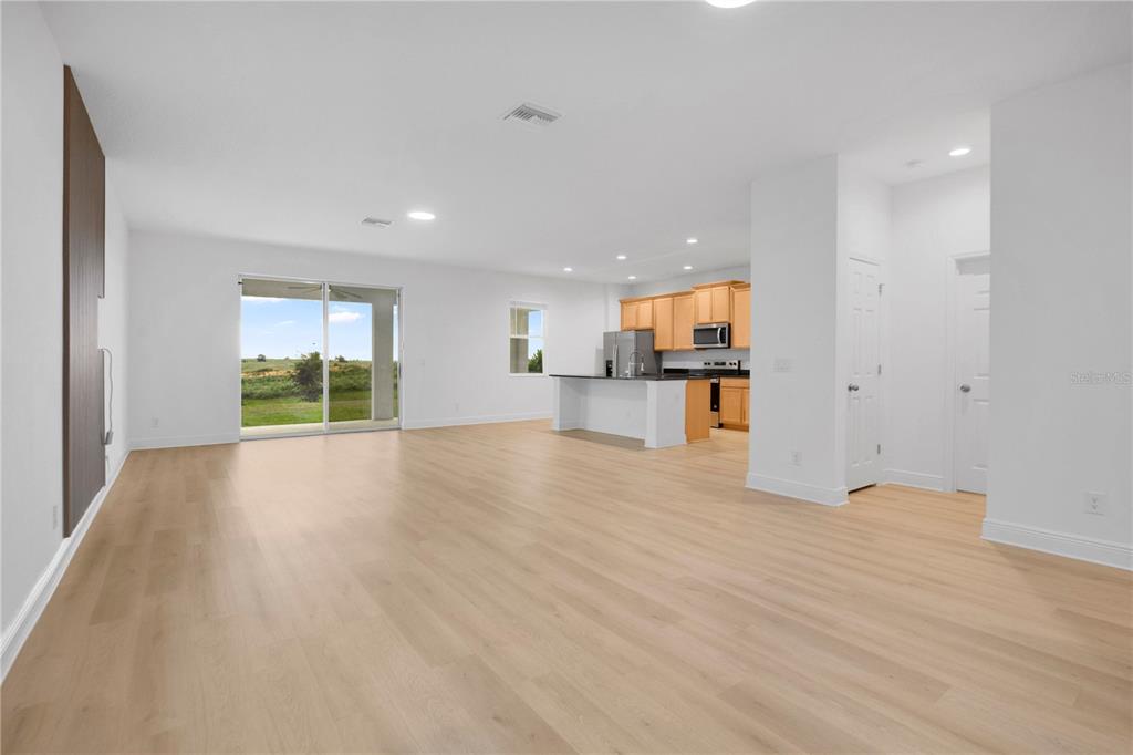 An open-concept living area with light wood flooring, a kitchen with wooden cabinets, and sliding doors — 7767 TRAPANI LOOP, CLERMONT, FL
