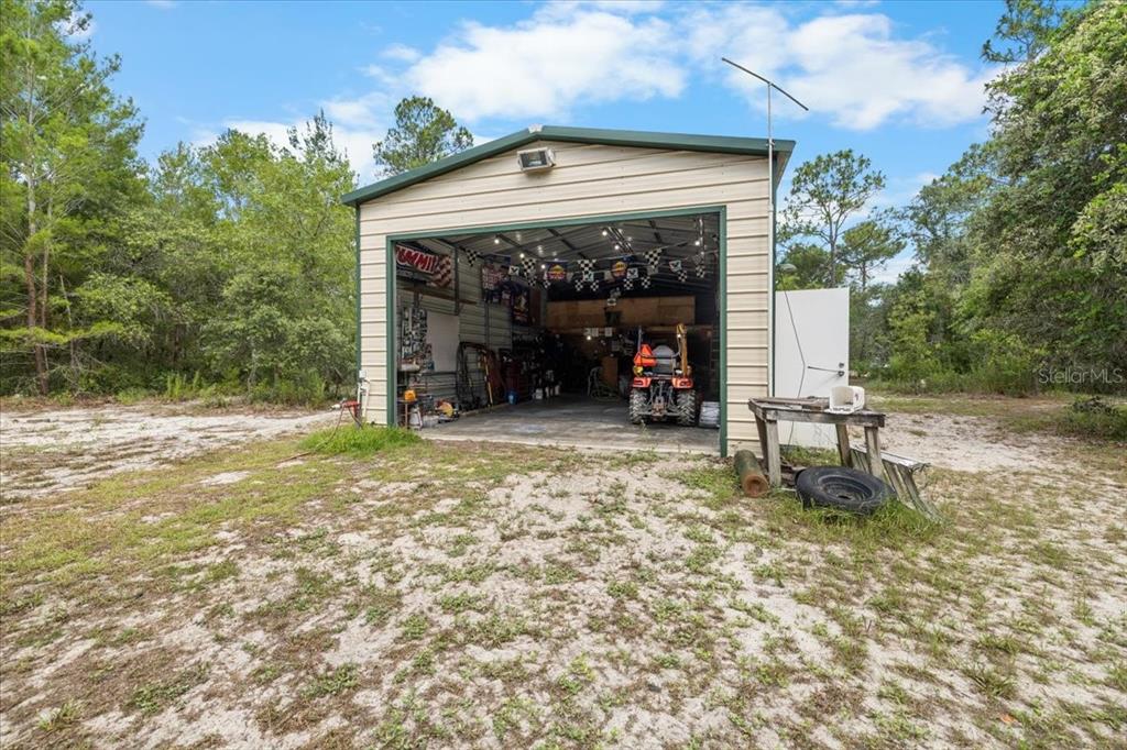 A detached metal garage sits on a sandy lot surrounded by trees — 15624 PEACE BOULEVARD, SPRING HILL, FL