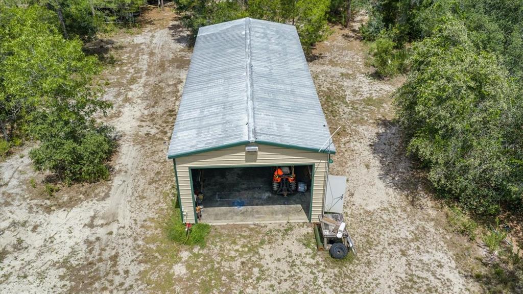 An aerial view of a detached metal garage with an open bay and a tractor inside — 15624 PEACE BOULEVARD, SPRING HILL, FL