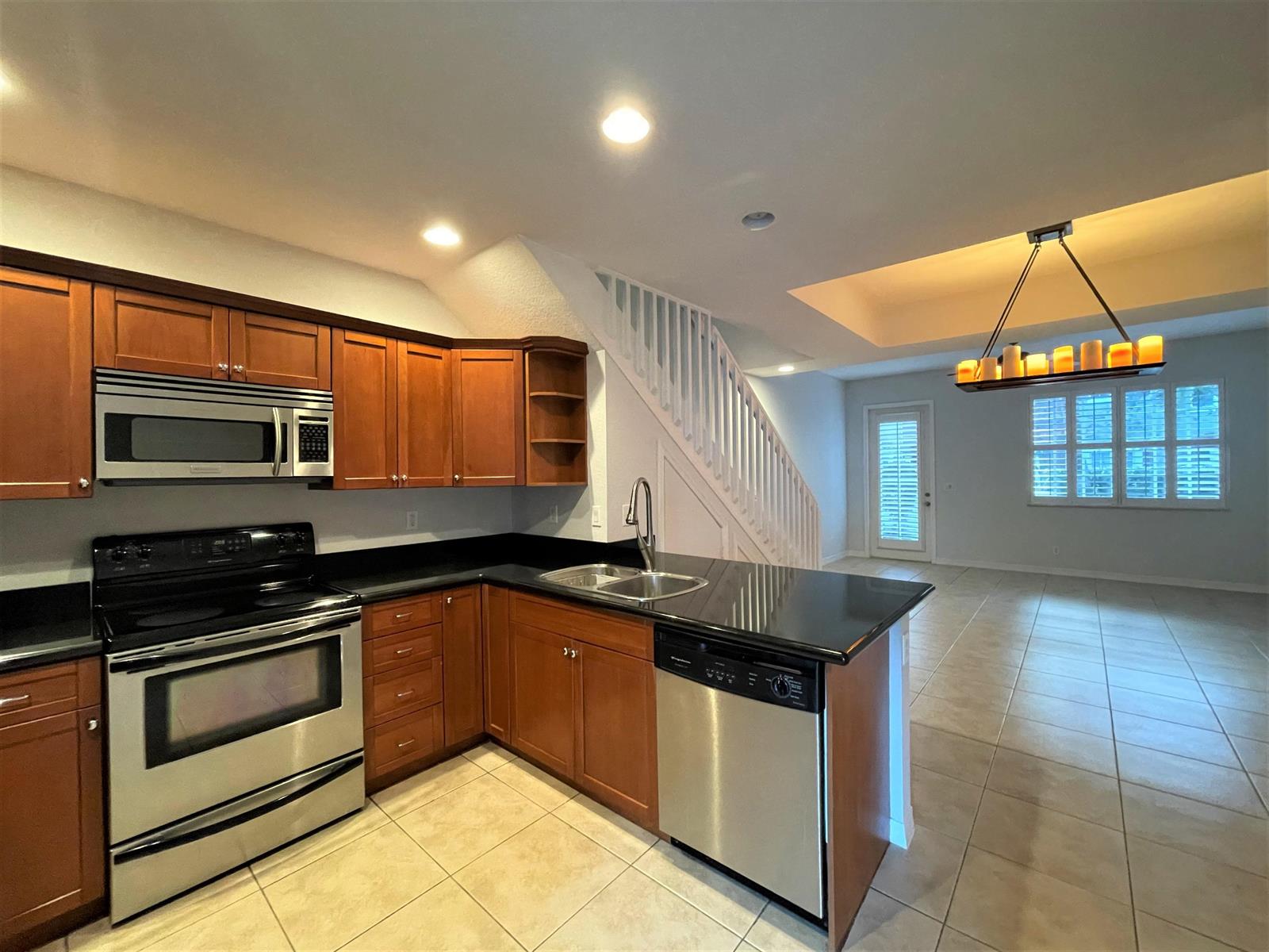 A kitchen with wood cabinets, black countertops, and stainless steel appliances next to a staircase — 602 S Federal Highway # 5, FL 33460, FL