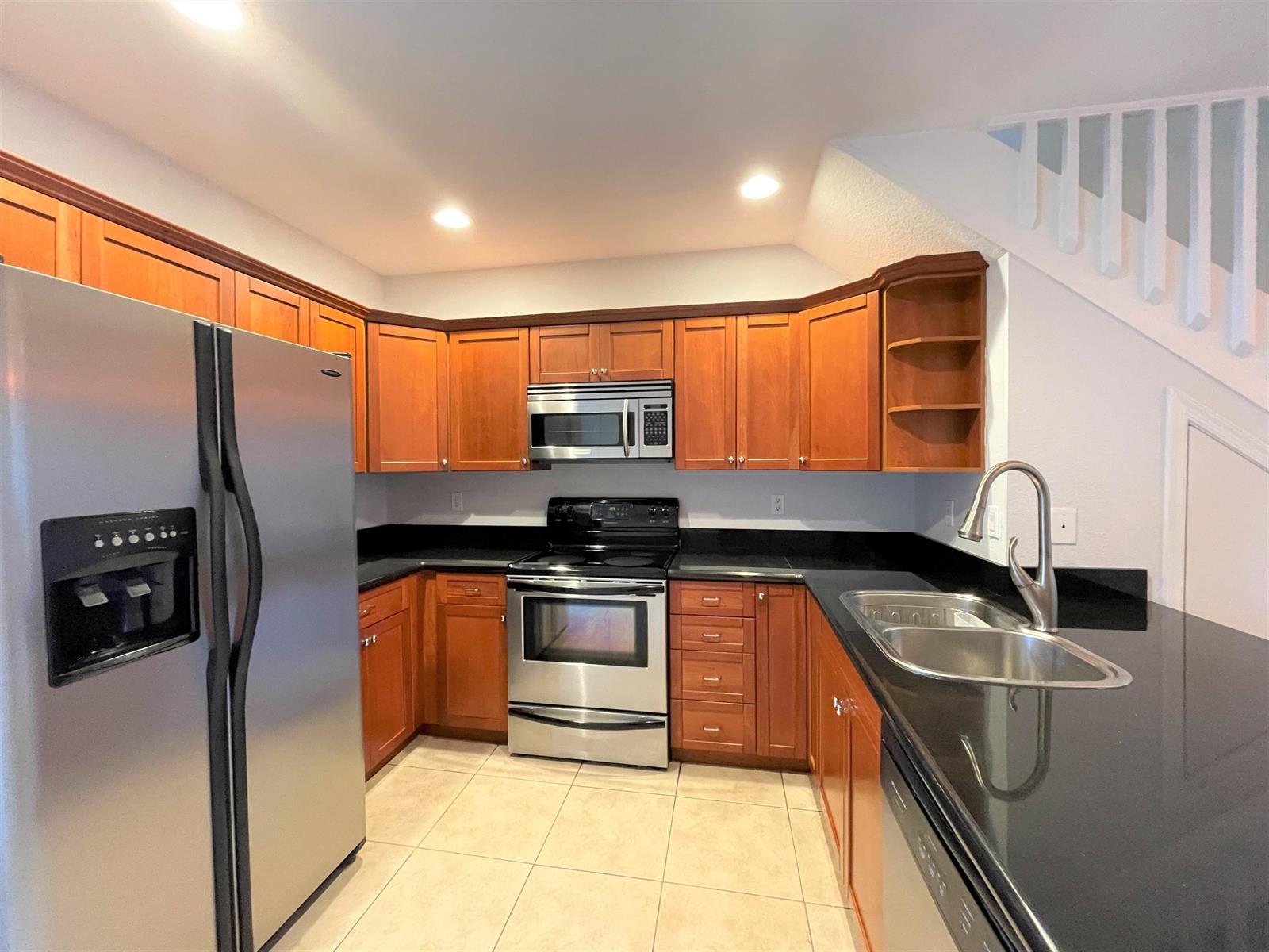 A kitchen features wood cabinets, black countertops, stainless steel appliances, and light-colored tile flooring — 602 S Federal Highway # 5, FL 33460, FL