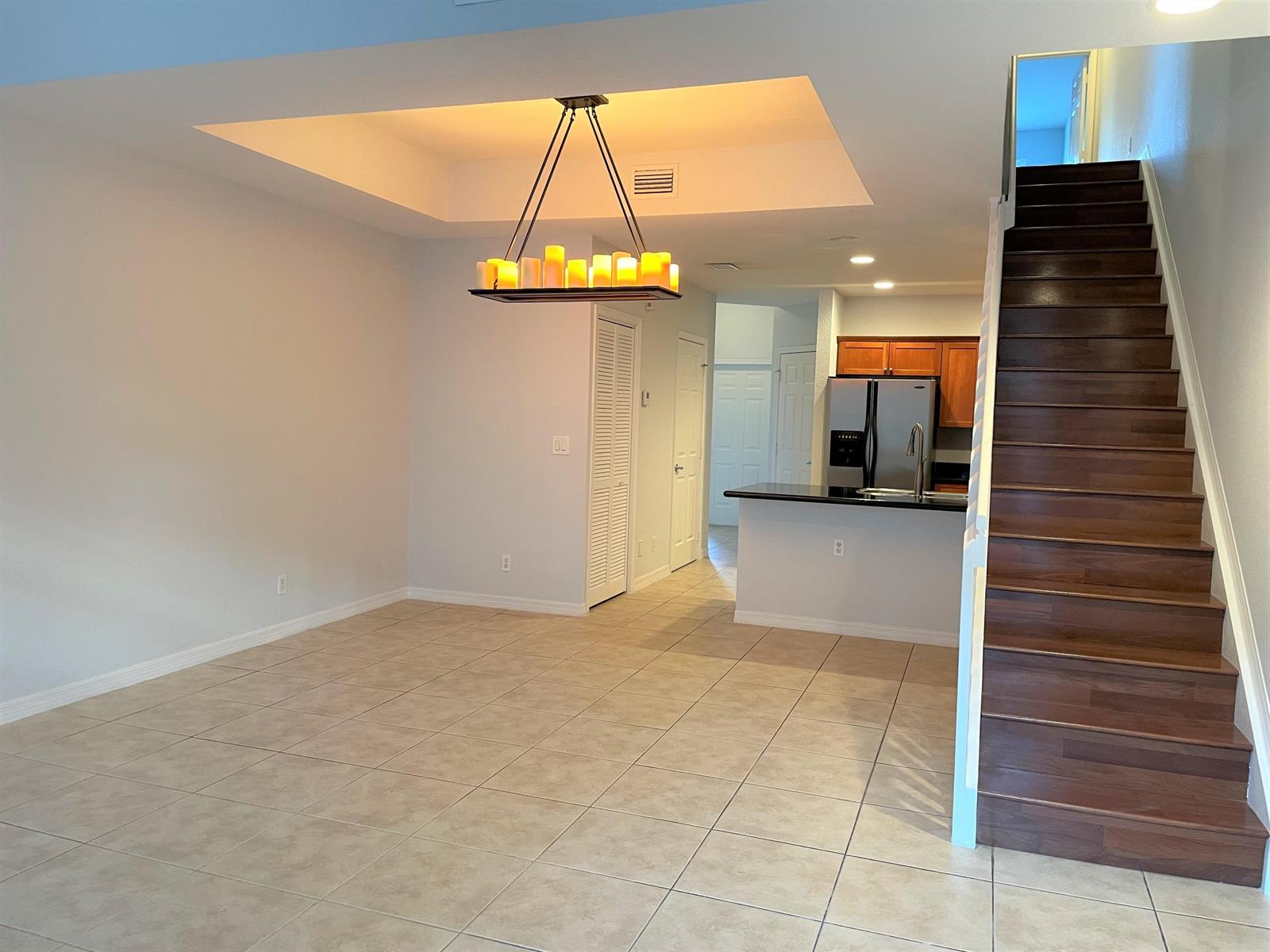 An open-concept dining area with a tray ceiling, chandelier, tile floors, and wooden staircase — 602 S Federal Highway # 5, FL 33460, FL