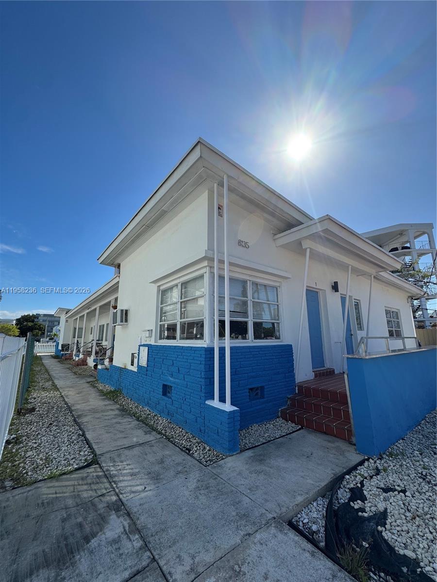 A low-angle exterior view of a white building with a blue brick base — 8135 Crespi Blvd, Miami Beach FL 33141, MIAMI BEACH, FL