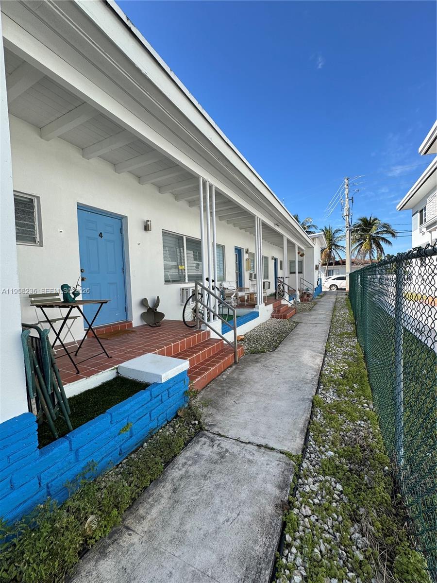 A row of white apartment units features blue doors, tiled porches, and a chain-link fence — 8135 Crespi Blvd, Miami Beach FL 33141, MIAMI BEACH, FL