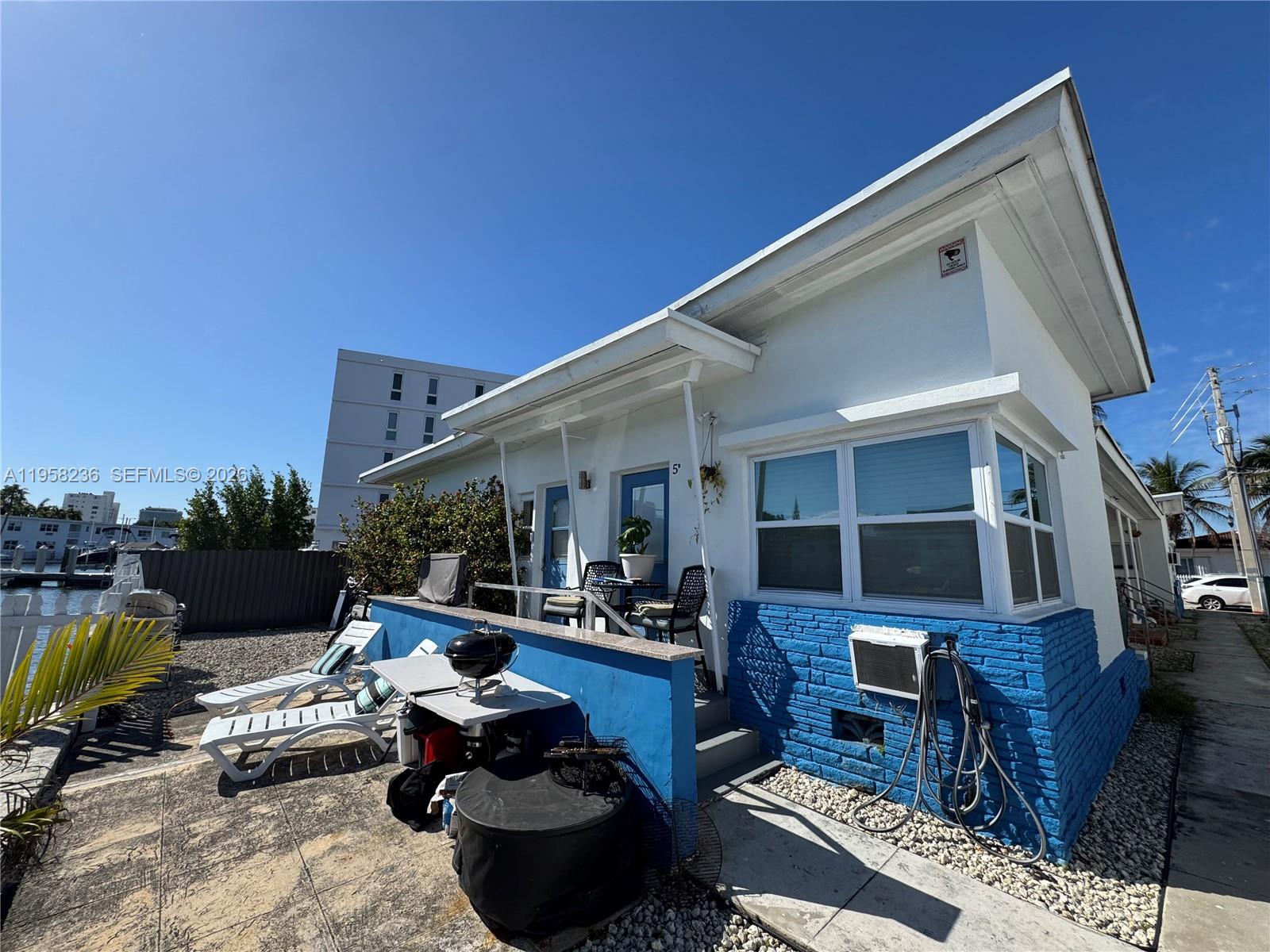 A white and blue cottage features a patio with lounge chairs and a small grill — 8135 Crespi Blvd, Miami Beach FL 33141, MIAMI BEACH, FL