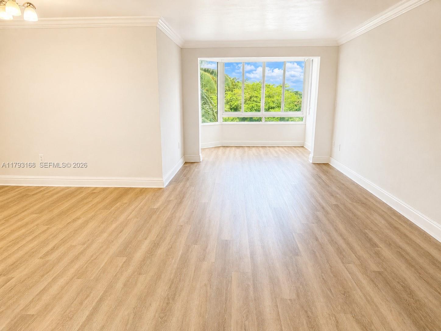 An empty room features light wood-look flooring, beige walls, and a large bay window — 8305 SW 152nd Ave # 411, Miami FL 33193, MIAMI, FL