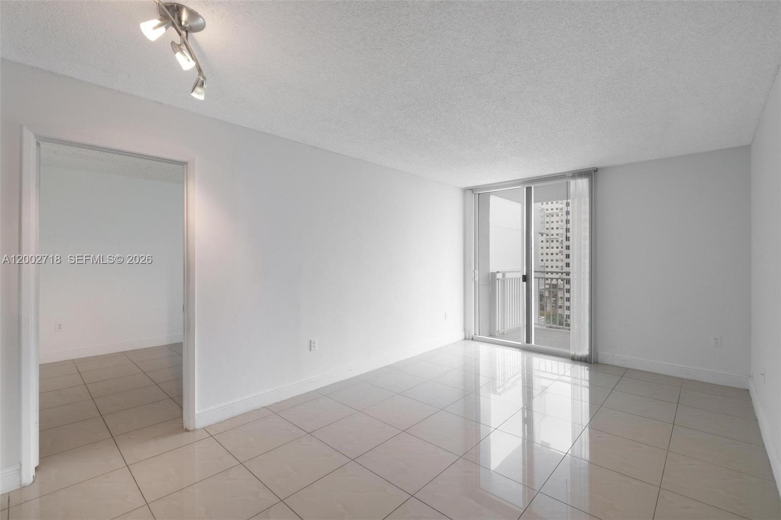 A bright, empty room features white walls, large beige floor tiles, and a sliding glass door — 800 N Miami Ave # 1110, Miami FL 33136, MIAMI, FL