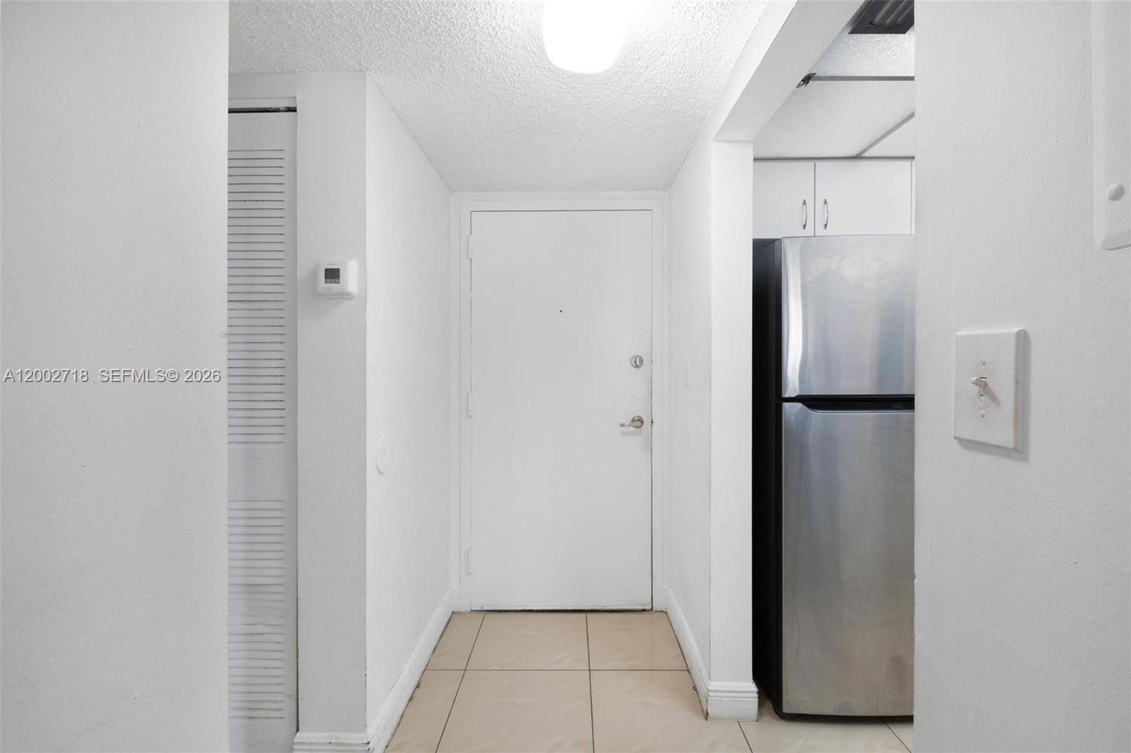 A hallway features a white entry door, tile flooring, and a stainless steel refrigerator — 800 N Miami Ave # 1110, Miami FL 33136, MIAMI, FL