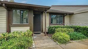 A tan-sided house exterior features a front door with a security screen and landscaping — 5911 39TH AVENUE W, BRADENTON, FL