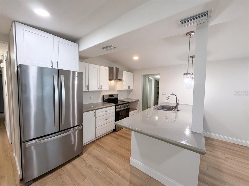 A kitchen features white cabinets, stainless steel appliances, a gray island, and light wood flooring — 2905 E CHELSEA STREET, TAMPA, FL