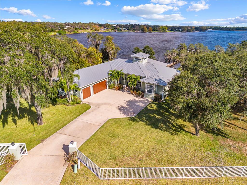 An aerial view shows a house with a metal roof, garage, and driveway by water — 7354 RED BEACH COURT, SEBRING, FL