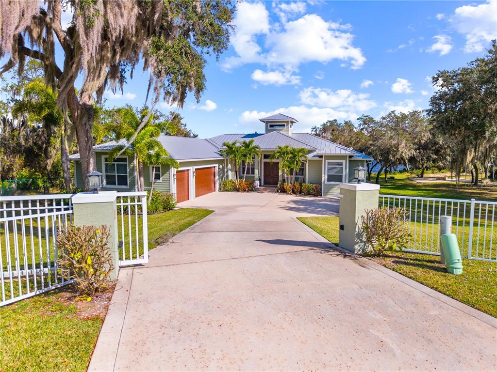 A green house with a metal roof and a concrete driveway behind a gated entrance — 7354 RED BEACH COURT, SEBRING, FL