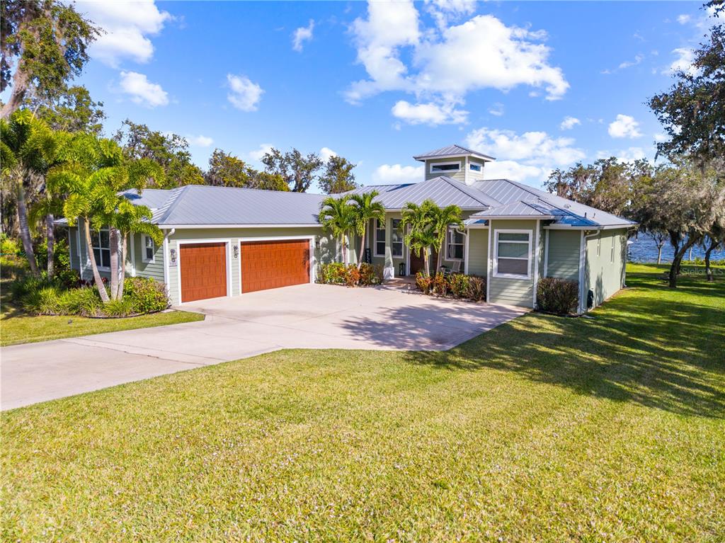 A single-story house with a metal roof, two-car garage, and palm trees on a lawn — 7354 RED BEACH COURT, SEBRING, FL