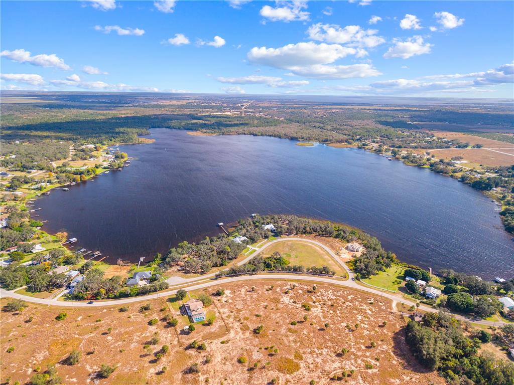 An aerial view shows a large lake surrounded by trees, residential properties, and open land — 7354 RED BEACH COURT, SEBRING, FL