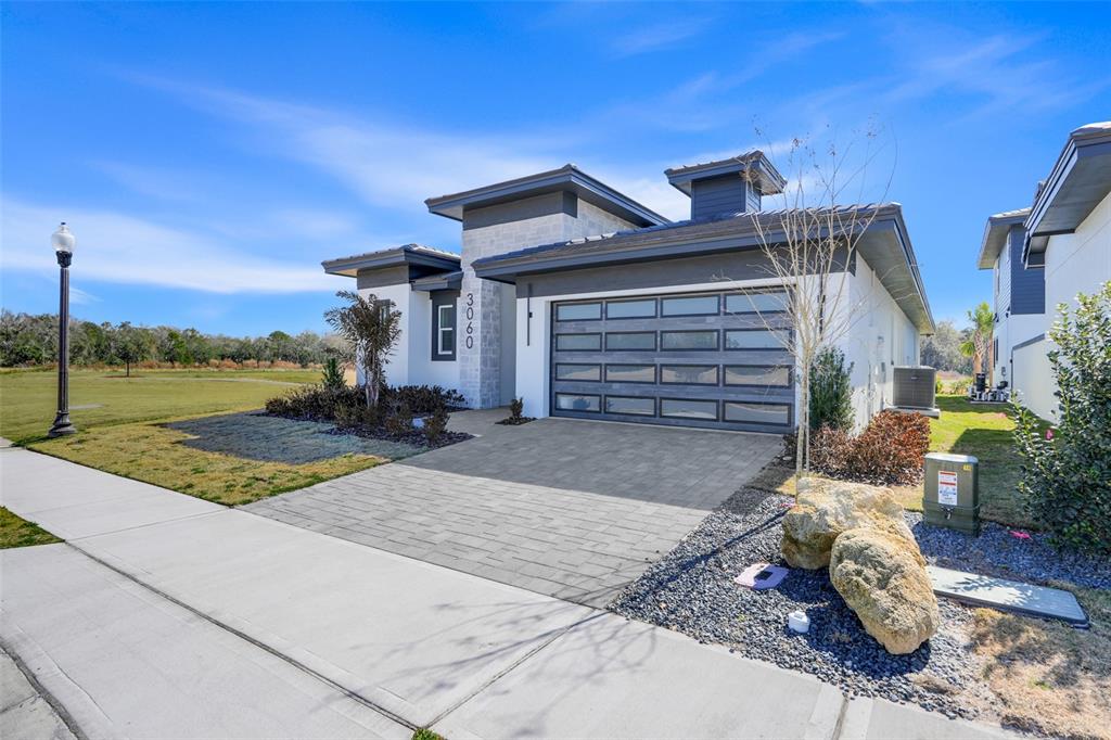 A modern single-story house features a stone facade, a multi-panel garage door, and a driveway — 3060 KENSINGTON AVENUE, DAVENPORT, FL
