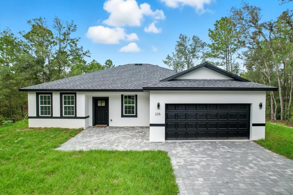 A single-story house with white stucco walls, black trim, and a paved driveway — 225 W DIEGO PLACE, CITRUS SPRINGS, FL