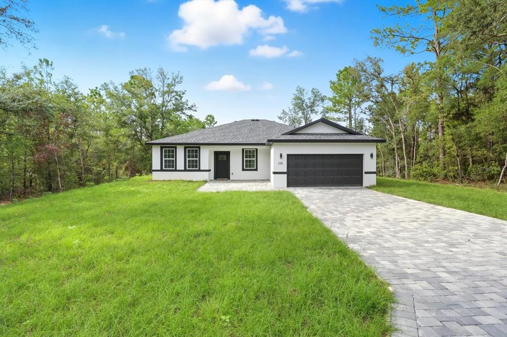 A single-story house with a white stucco exterior, black trim, and a paved driveway — 225 W DIEGO PLACE, CITRUS SPRINGS, FL