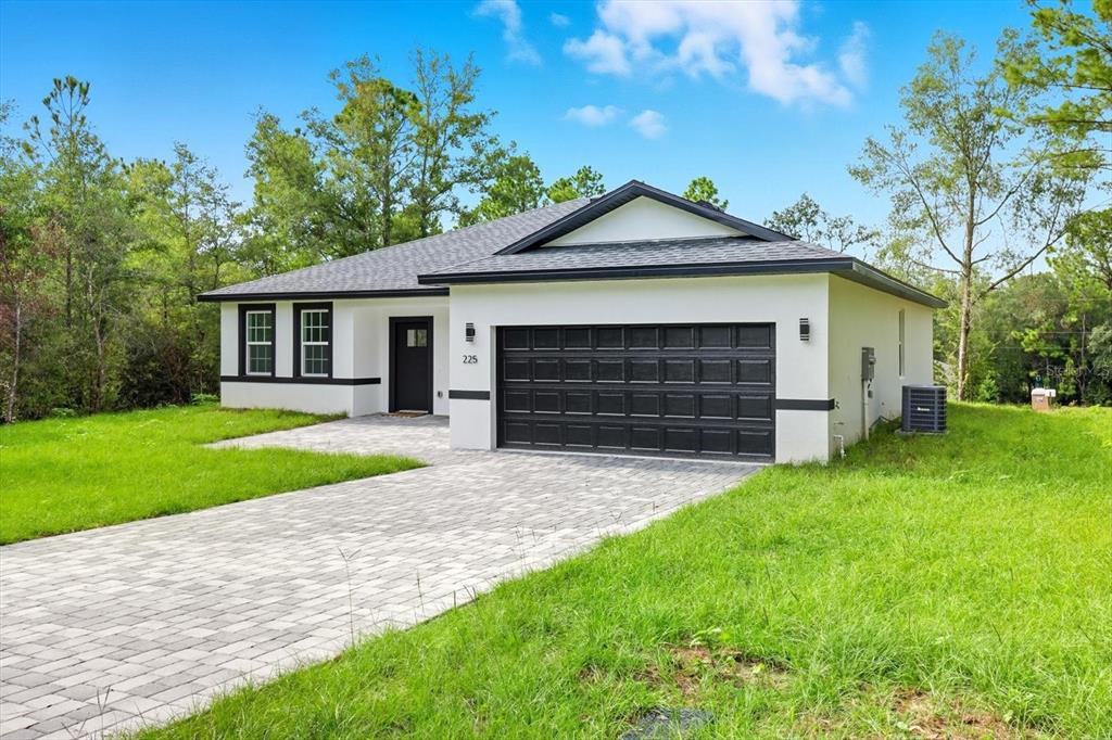 A single-story house with white stucco walls, a black garage door, and a paved driveway — 225 W DIEGO PLACE, CITRUS SPRINGS, FL