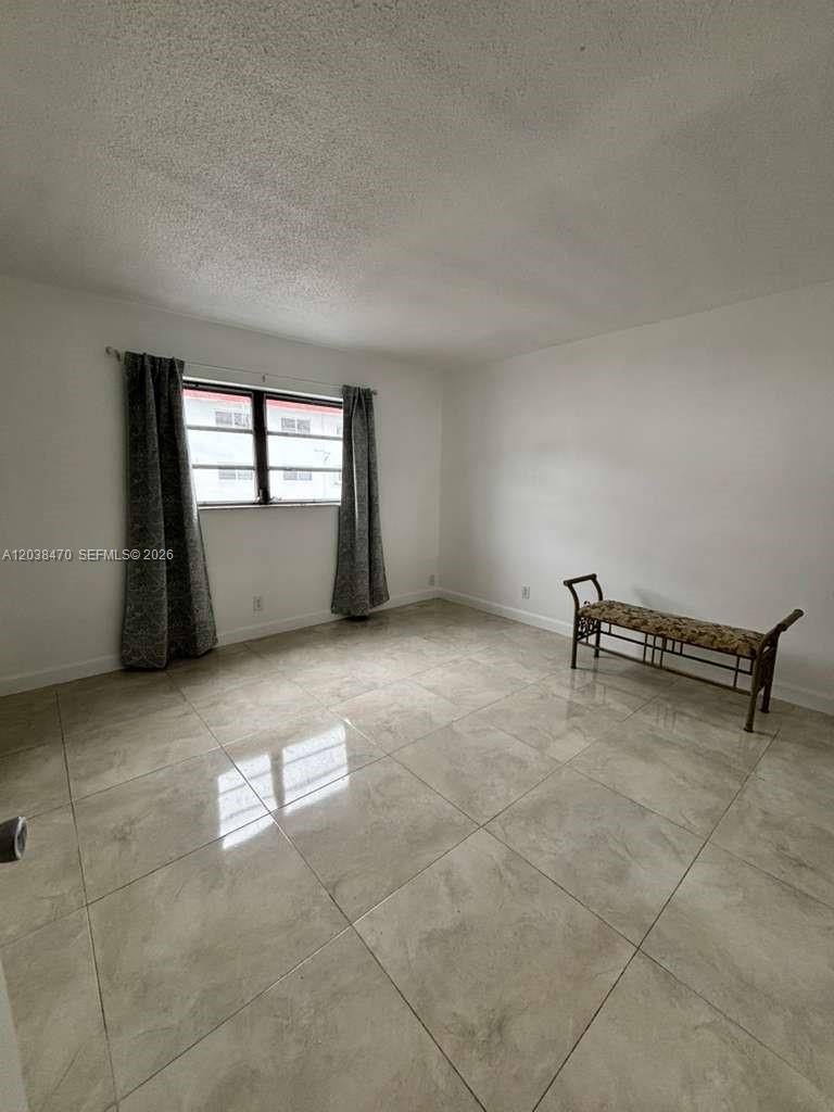 An empty room features white walls, light-colored tile flooring, and a window with curtains — 541 Blue Heron Dr # 215, Hallandale Beach FL 33009, HALLANDALE BEACH, FL