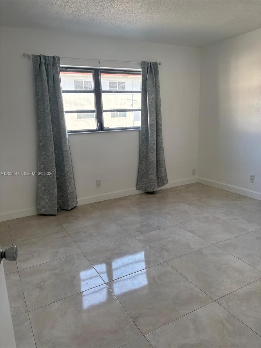 An empty bedroom features white walls, light-colored tile flooring, and a window with patterned curtains — 541 Blue Heron Dr # 215, Hallandale Beach FL 33009, HALLANDALE BEACH, FL