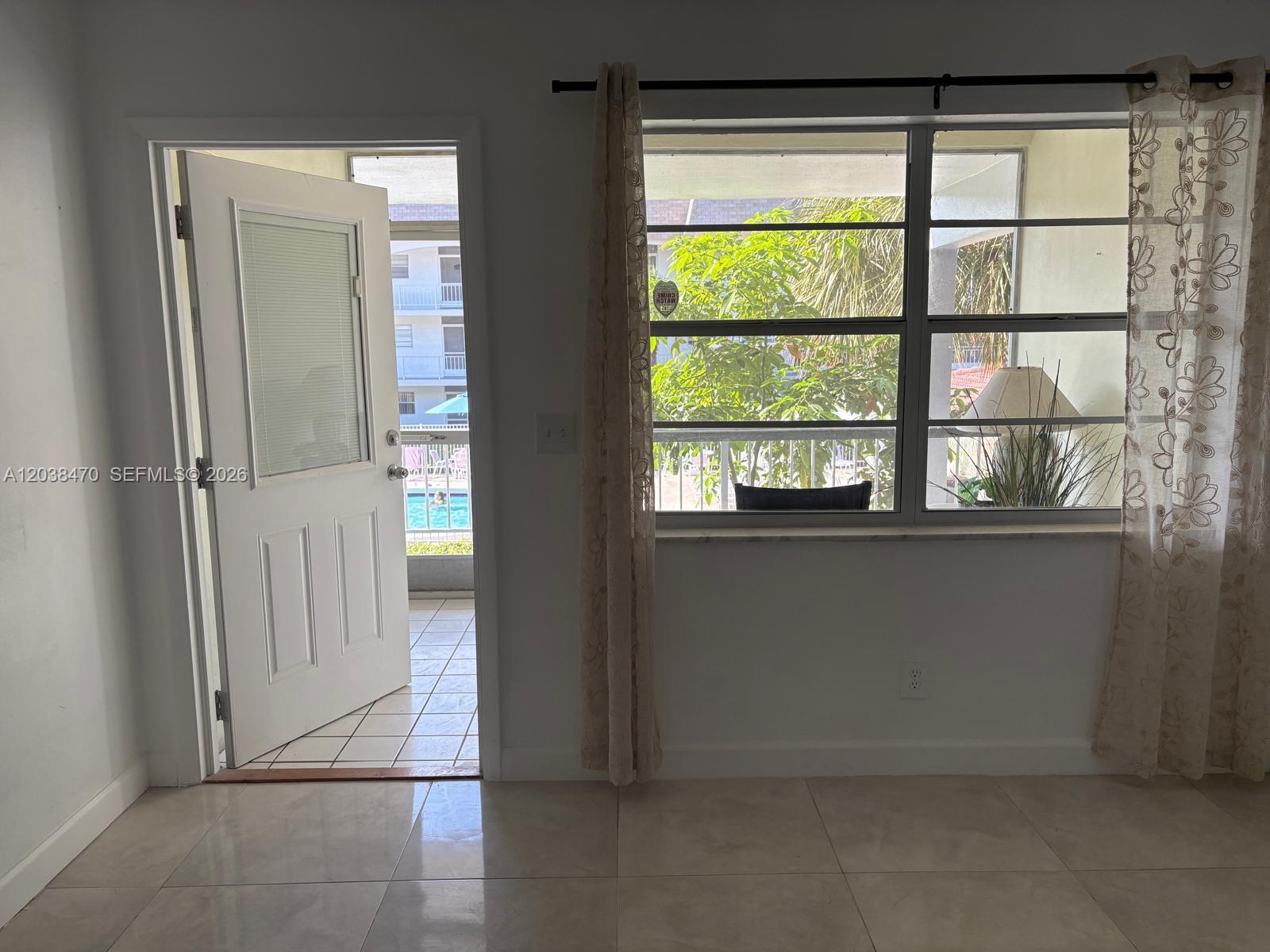 An interior room with tile flooring, an open door to a balcony, and a window — 541 Blue Heron Dr # 215, Hallandale Beach FL 33009, HALLANDALE BEACH, FL