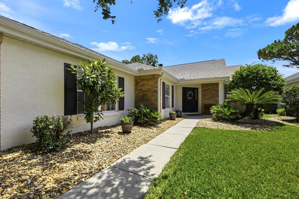 A single-story house with a beige stucco exterior, brick accents, and a concrete walkway — 1750 STAFFORD SPRINGS BOULEVARD, MOUNT DORA, FL