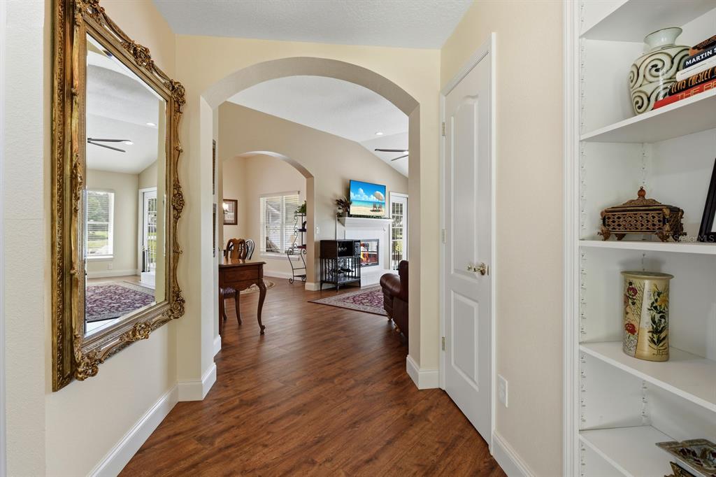 A hallway with wood-look flooring leads through an arched doorway into a living room — 1750 STAFFORD SPRINGS BOULEVARD, MOUNT DORA, FL