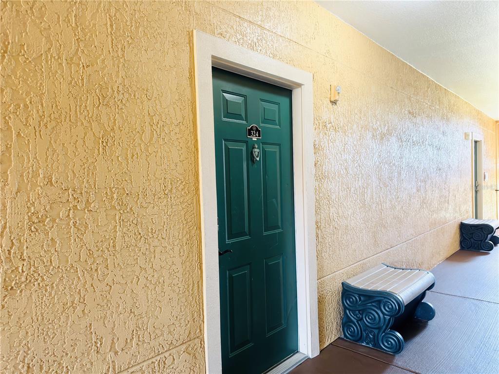 A green apartment door with a number plate and a bench sits in a hallway — 2721 VIA MURANO UNIT 324, CLEARWATER, FL