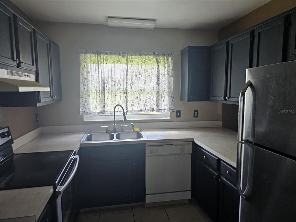 A kitchen features dark cabinets, a stainless steel sink, a white dishwasher, and a window — 569 HUNTER CIRCLE, KISSIMMEE, FL
