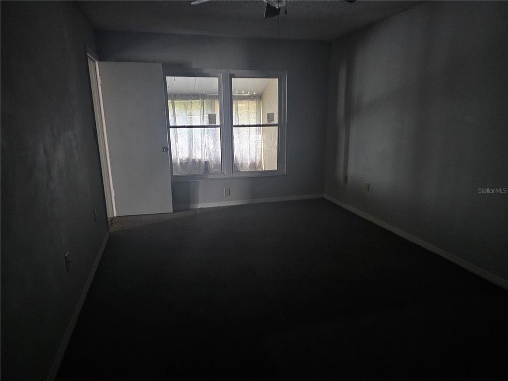An empty bedroom with gray walls, carpeted flooring, and two windows looking onto a porch — 569 HUNTER CIRCLE, KISSIMMEE, FL