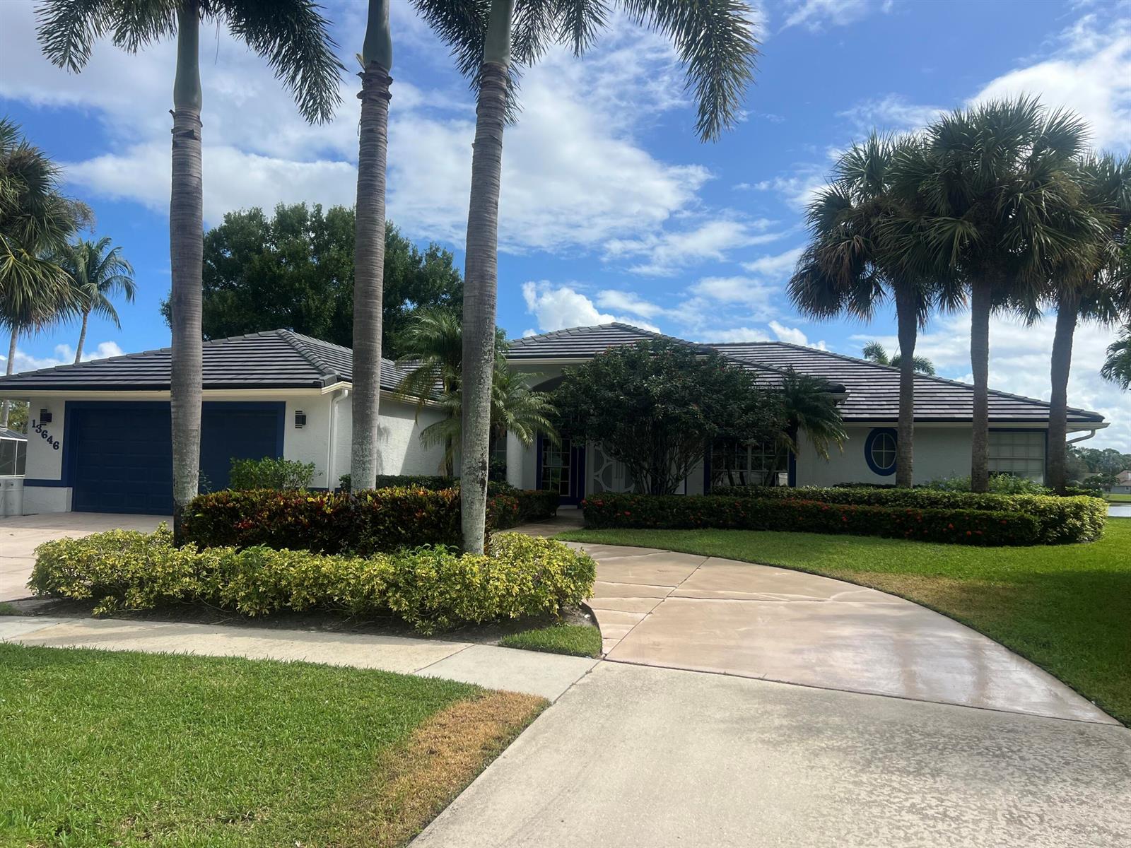 A single-story house with a dark tile roof, blue garage doors, and several palm trees — 13646 Callington Drive, Wellington FL 33414, WELLINGTON, FL