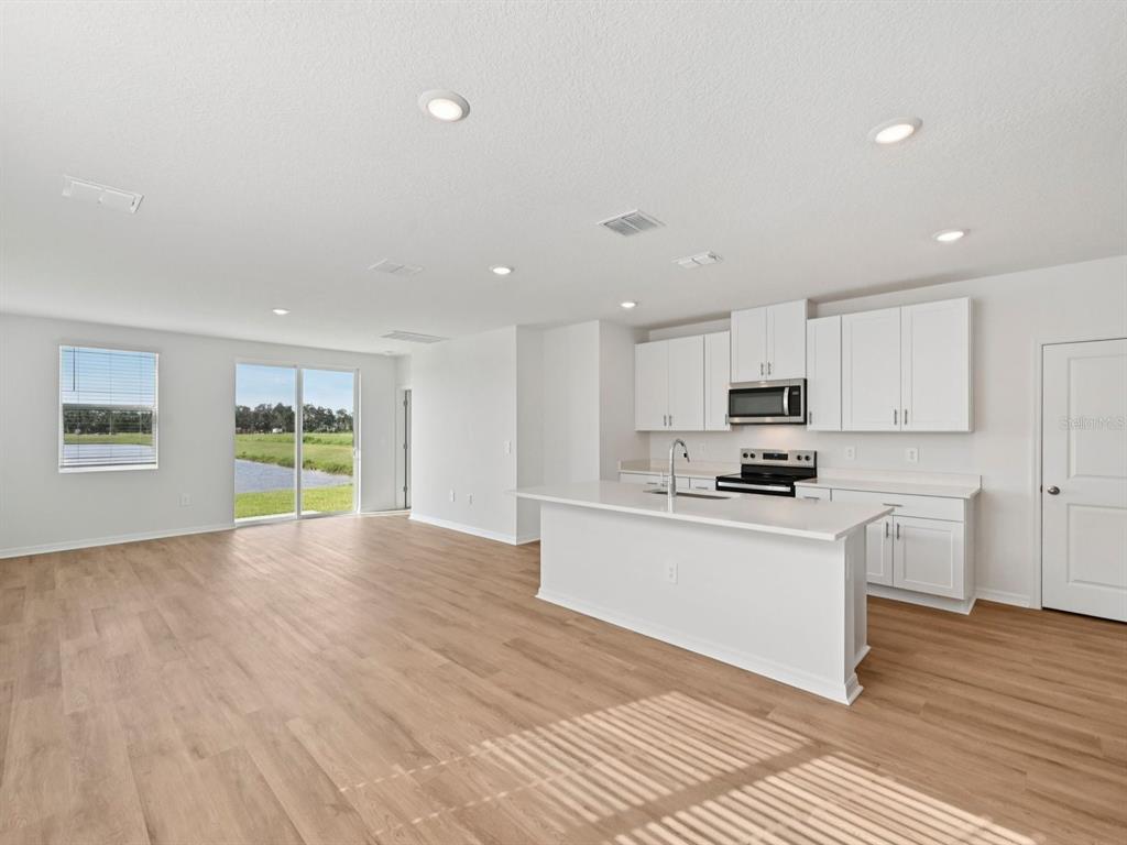 A kitchen with white cabinets and a center island opens to a living area — 7821 GILCHRIST SPRINGS DRIVE, PARRISH, FL