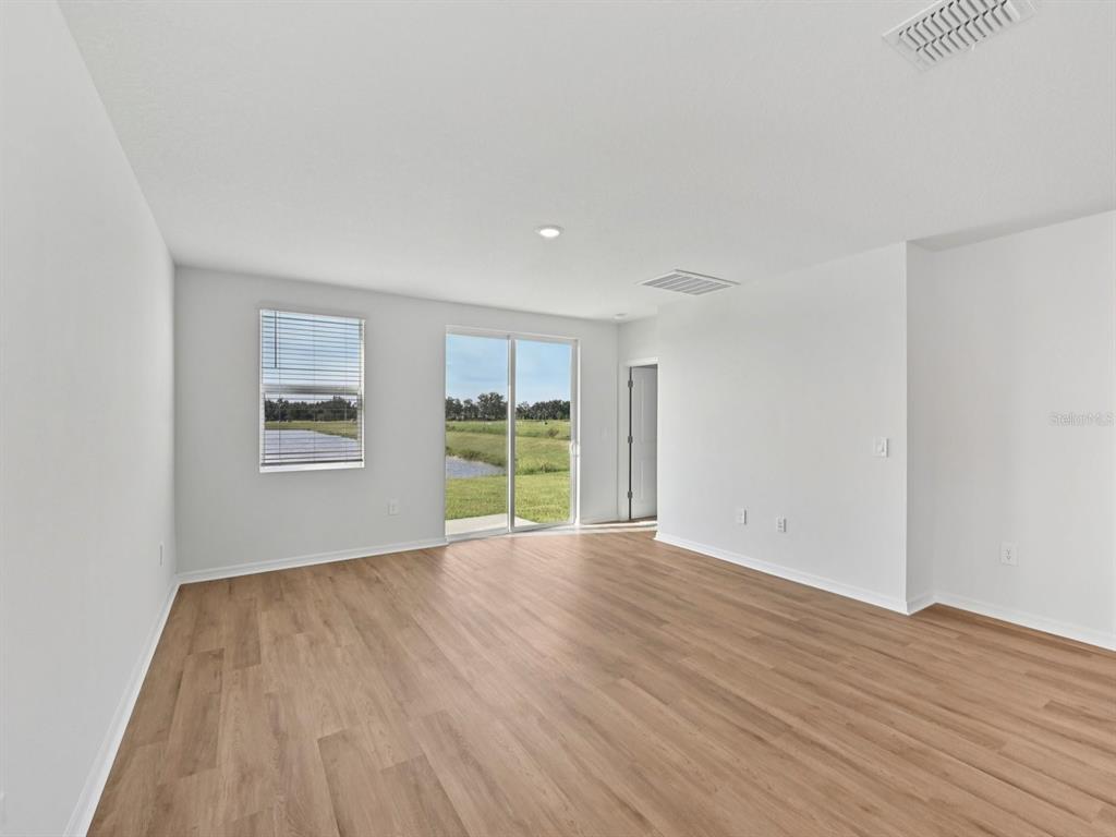 An empty room with light wood-look flooring, white walls, and a sliding glass door to outdoors — 7821 GILCHRIST SPRINGS DRIVE, PARRISH, FL