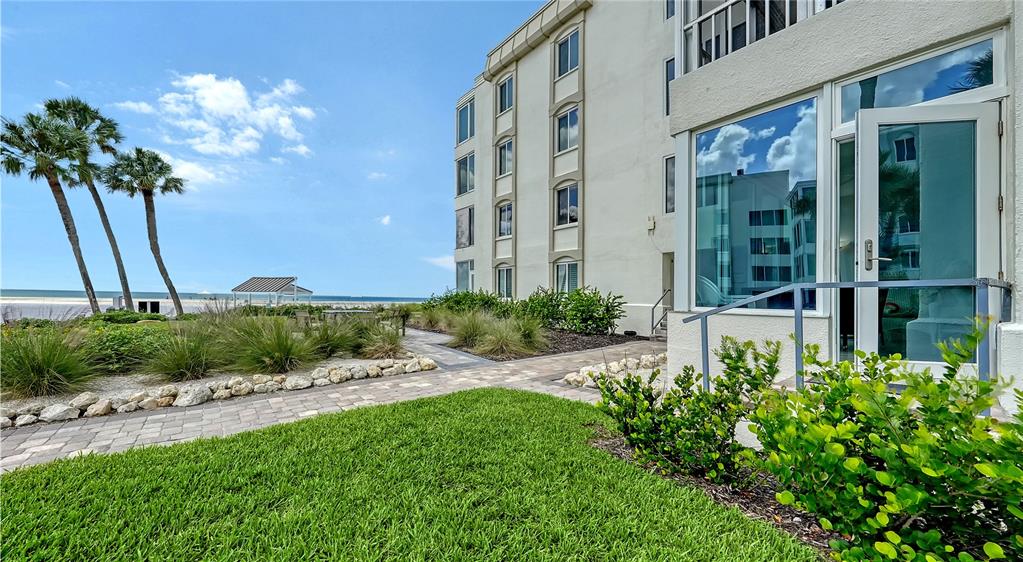 A paved walkway leads past a building exterior toward a beach with palm trees — 6144 MIDNIGHT PASS ROAD UNIT 2N, SARASOTA, FL