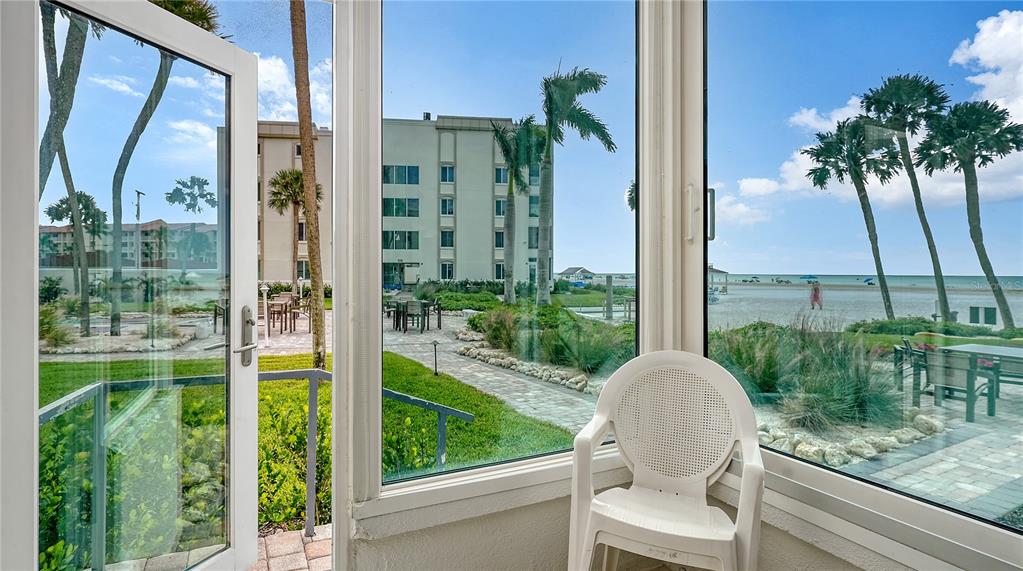 A white plastic chair sits in a sunroom looking out toward a beach and palm trees — 6144 MIDNIGHT PASS ROAD UNIT 2N, SARASOTA, FL