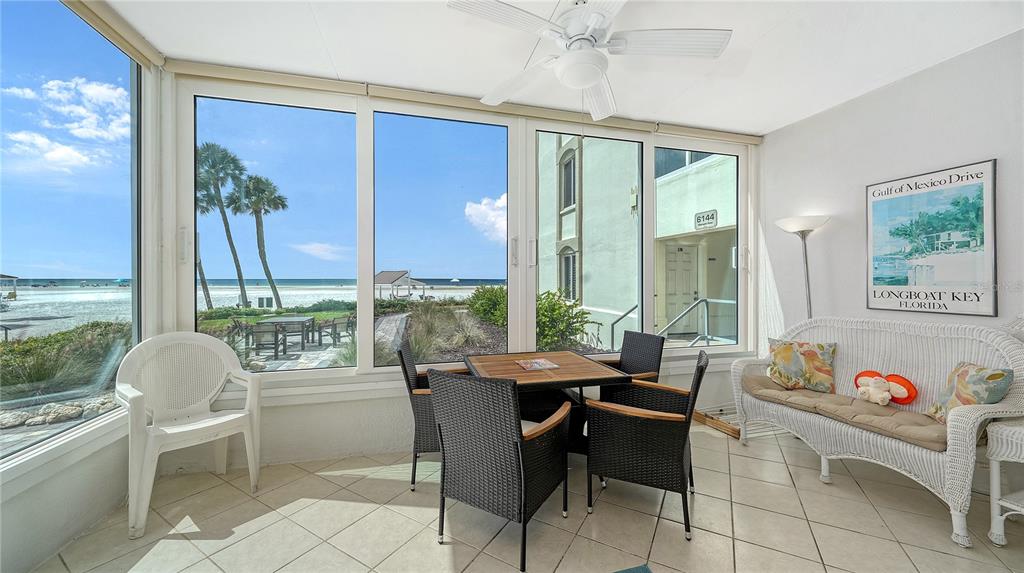 A sunroom features tile floors, a dining set, wicker furniture, and large windows overlooking the beach — 6144 MIDNIGHT PASS ROAD UNIT 2N, SARASOTA, FL
