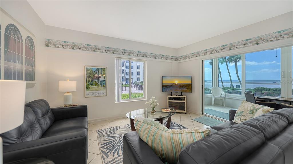 A living room features two black leather sofas, a glass coffee table, and ocean views — 6144 MIDNIGHT PASS ROAD UNIT 2N, SARASOTA, FL